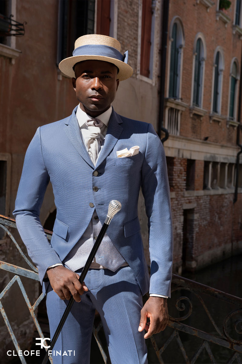 African American Man Fashion in New York. Dressing formally in blue suit,  black shirt, bow tie, wearing earring, black man with afro hairstyle stands  against light pole on street, looks forward. Stock